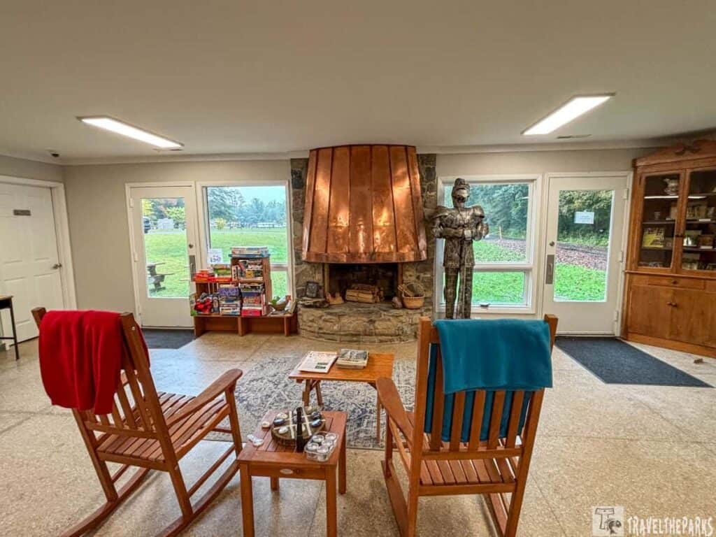 Visitor center room with stone fireplace, copper hood, metal sculpture, rocking chairs, and games shelf.

