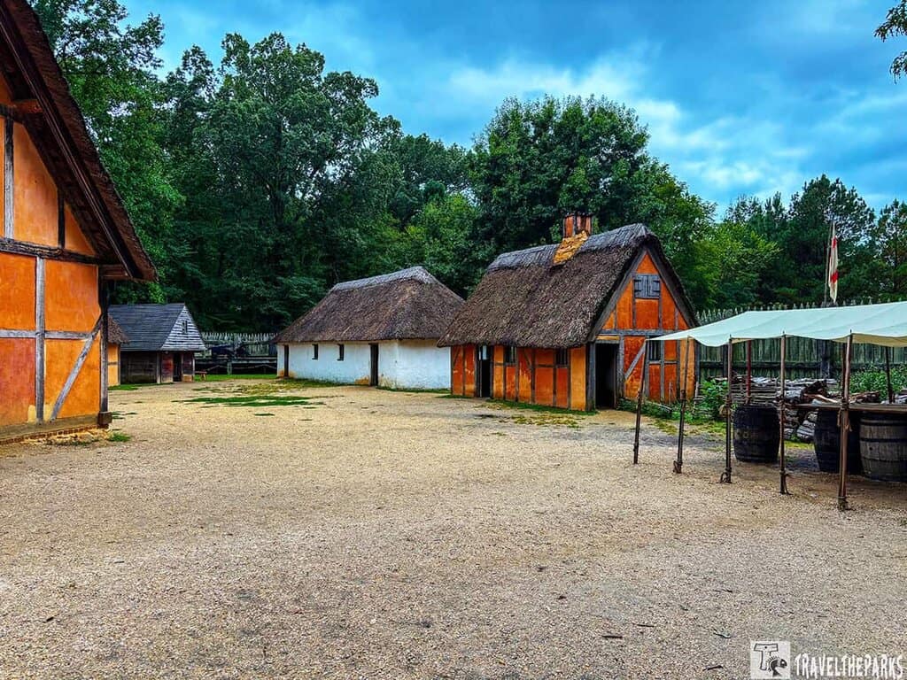 Historic Jamestown Settlement Fort James thatched-roof buildings and timber frames surround a sandy courtyard.