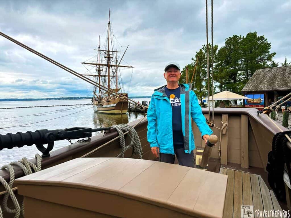 Person standing on a historic ship's deck, with the Susan Constant sailing ship docked in the background under an overcast sky.