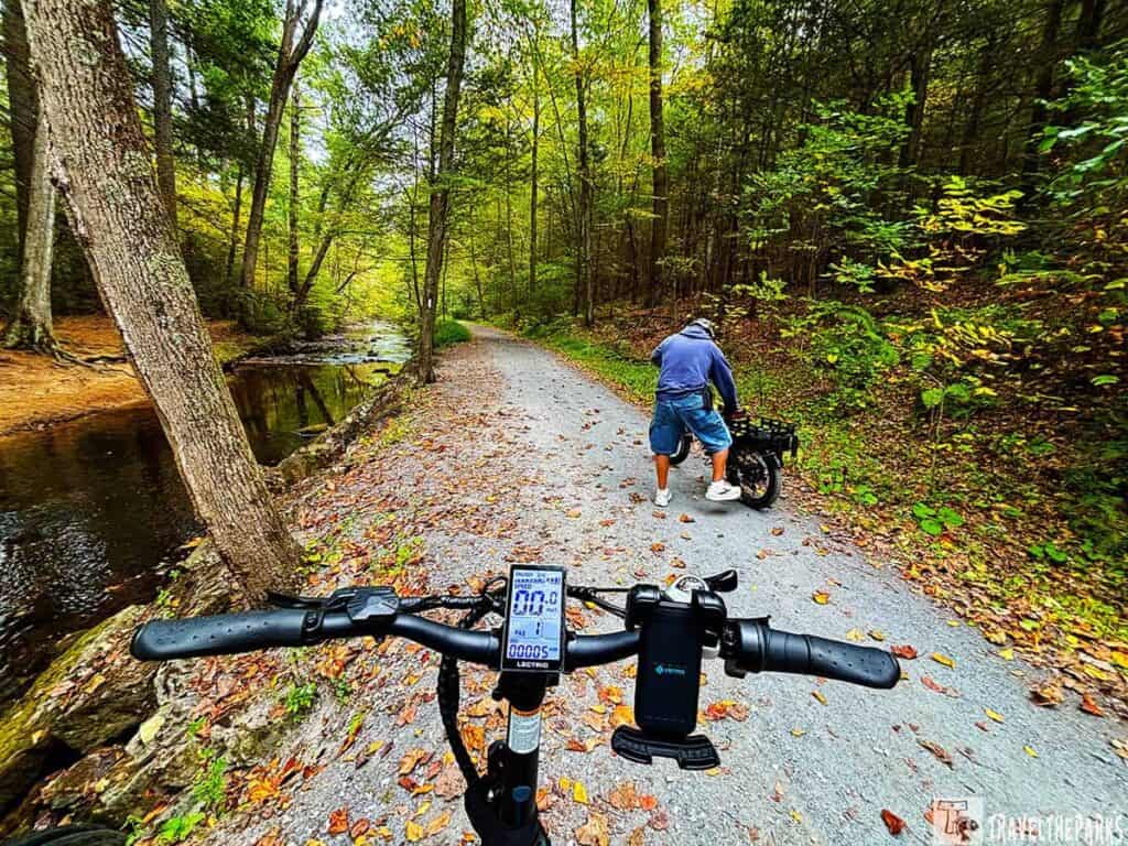 View from an electric bicycle on a wooded trail next to a creek in autumn.

