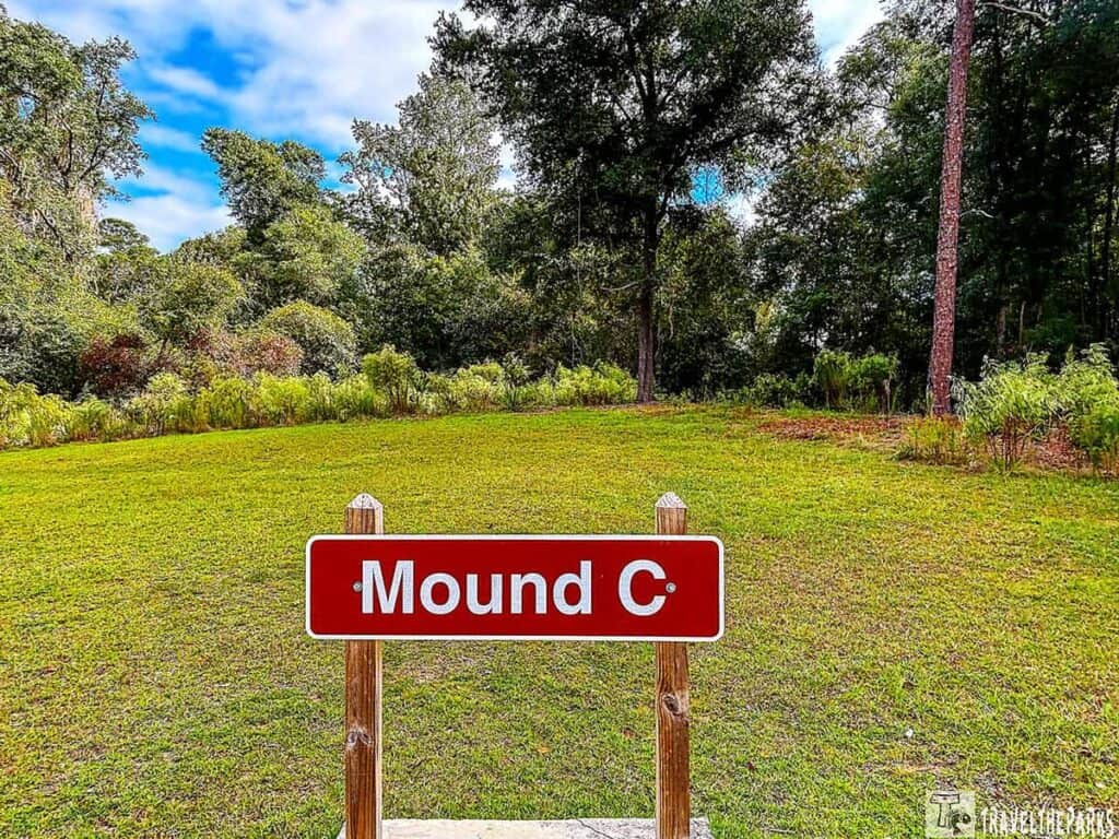 A sign labeled "Mound C" at Kolomoki Mounds State Park, surrounded by green grass and dense trees.
