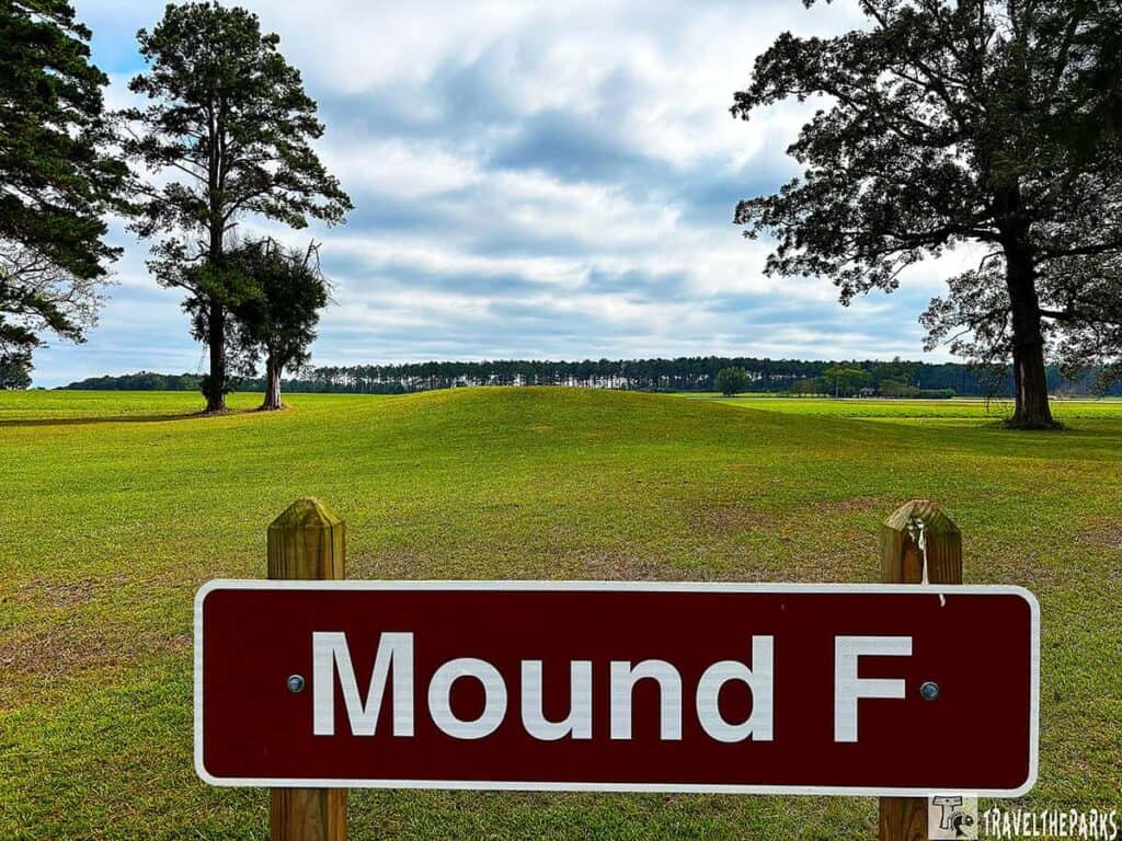 A sign reading "Mound F" at Kolomoki Mounds State Park with grassy fields and trees.

