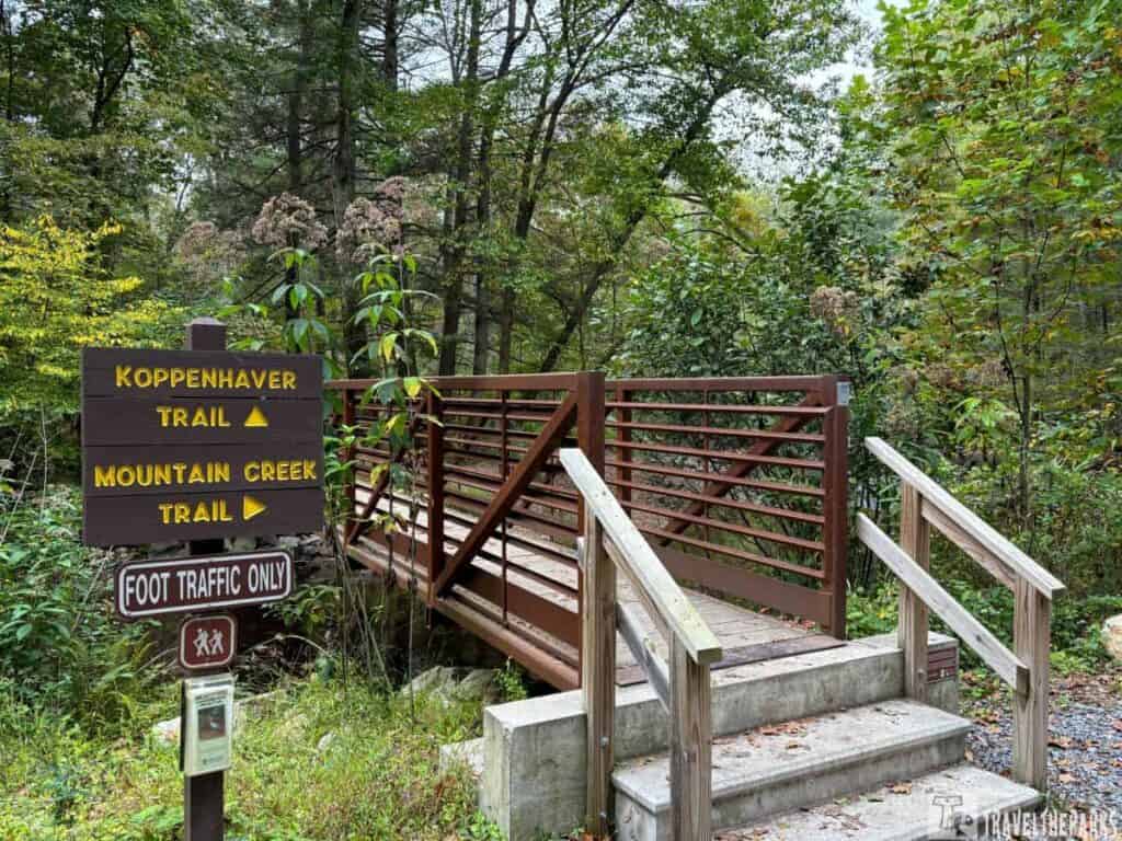 A wooden bridge in a forest with trail signs for Koppenhaver and Mountain Creek trails.