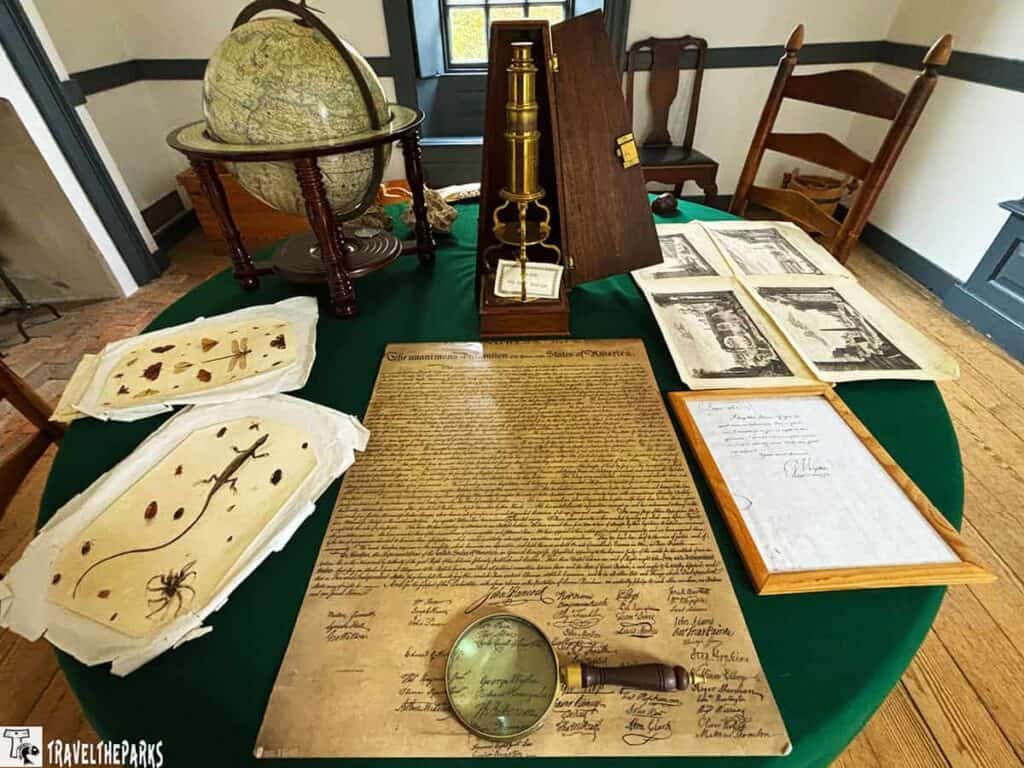 Historical display with a globe, microscope, insect specimens, and replica Declaration of Independence on a green table.