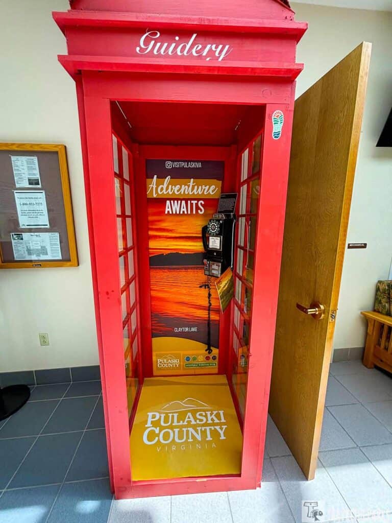 Red booth labeled "Guidery" with a sunset backdrop and the words "Adventure Awaits," featuring a vintage phone.

