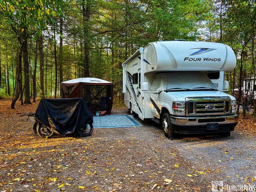 Motorhome and camping setup at Pine Grove Furnace State Park with trees and fallen leaves.