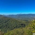 Cumberland Gap-Pinnacle Overlook-Panoramic view of a forested mountain range under a clear blue sky, with distant water reflections and hints of fall foliage.