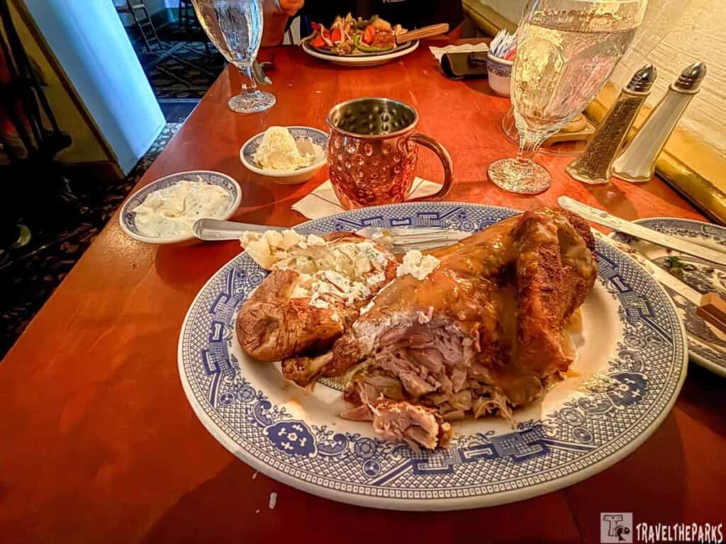 Dining table with a plate of roasted duck, mashed potatoes, and sides, alongside drinks and cutlery.