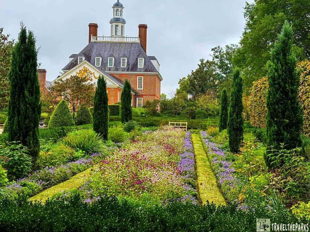 A formal garden with flower beds and hedges leading to a stately building with a cupola.