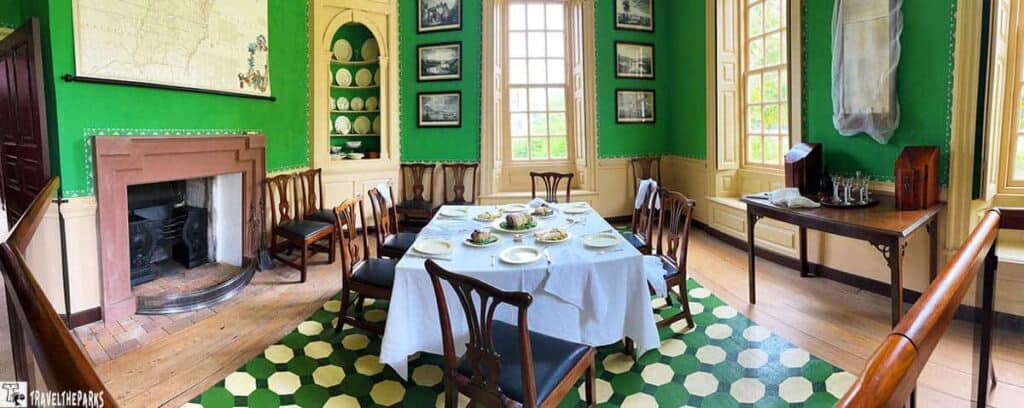 Dining room in the Wythe House with green walls, a fireplace, and a table set for dining.