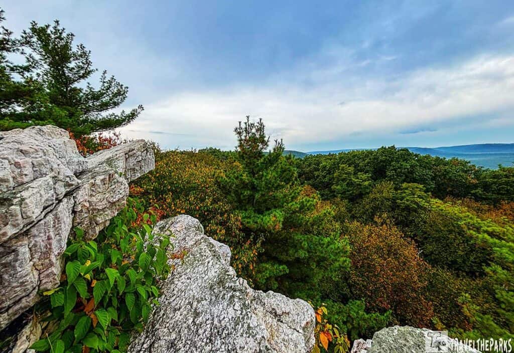 In Pine Grove Furnace State Park a view from Pole Steeple Overlook with rocky foreground and a dense forest below under a cloudy sky.