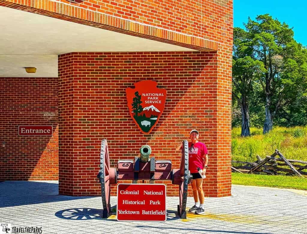 Entrance to Yorktown Battlefield with a brick wall, a historic cannon, and National Park Service sign.

