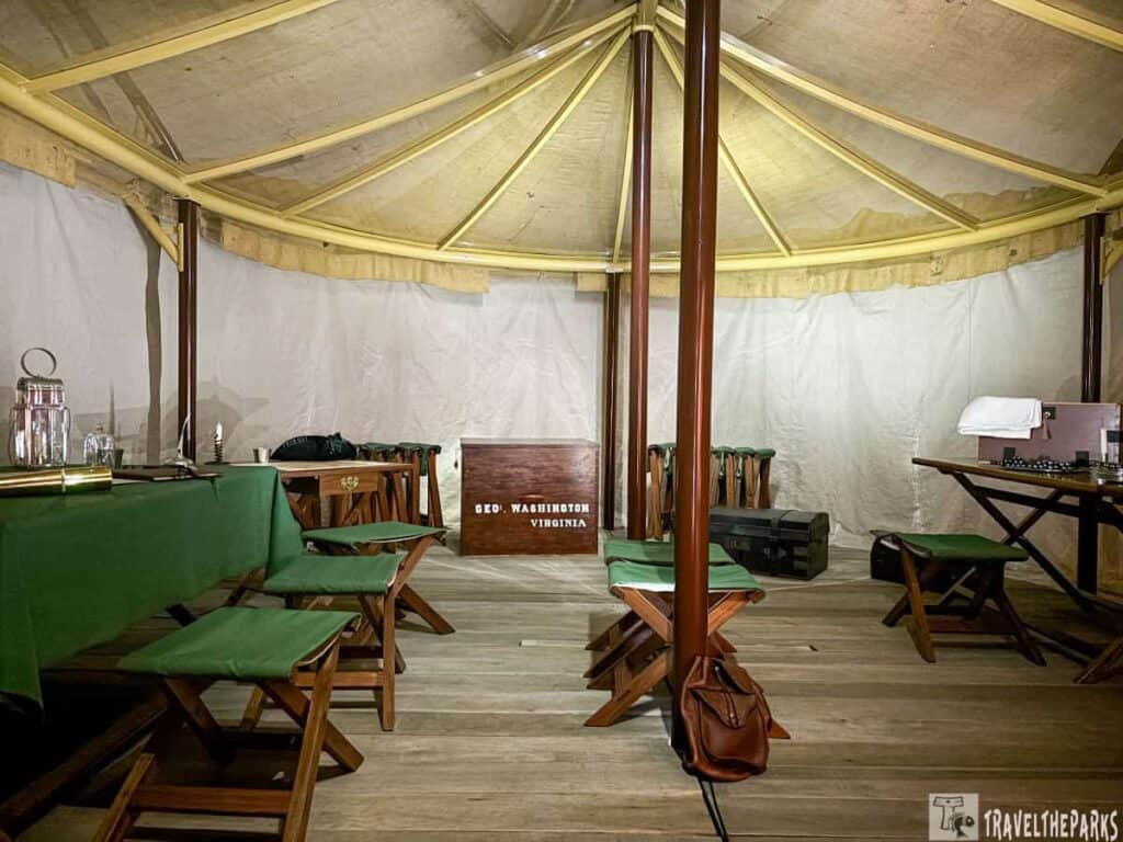 Interior of a historical military tent with wooden furniture and a "Geo. Washington Virginia" chest.