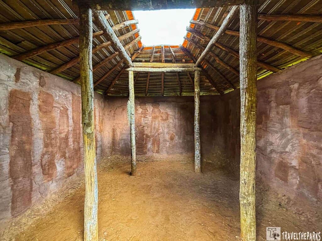 Interior of a historical structure at Kolomoki Mounds with clay walls, wooden poles, and an open-topped wooden ceiling.

