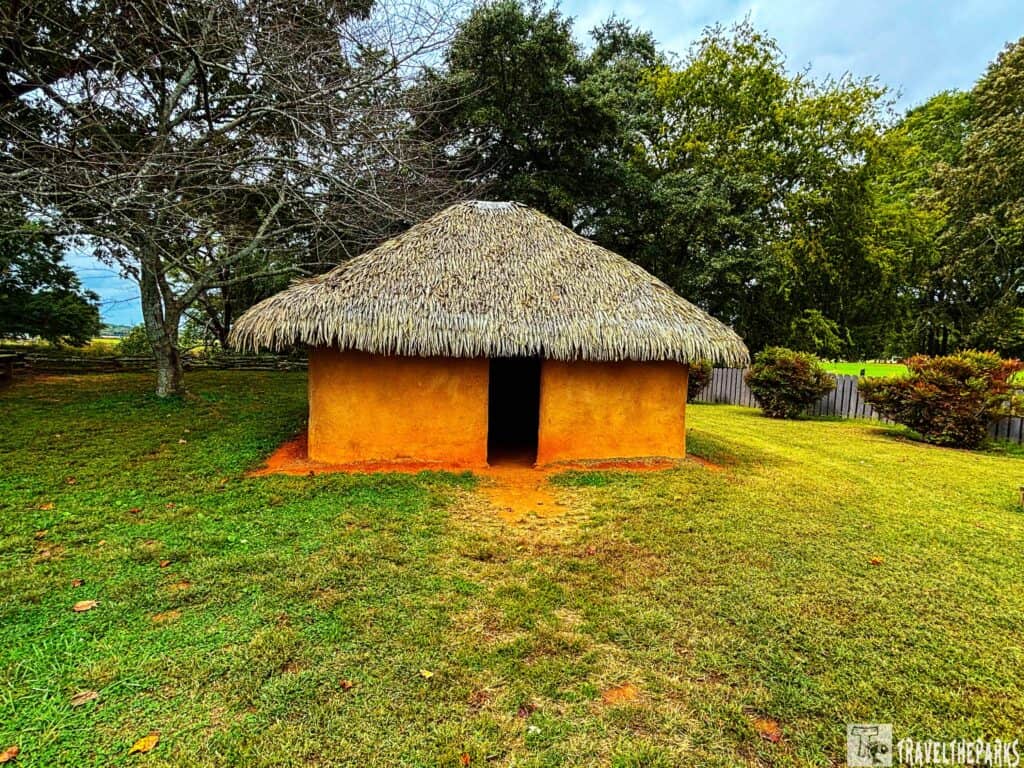 Traditional wattle and daub house with thatched roof on grassy land.