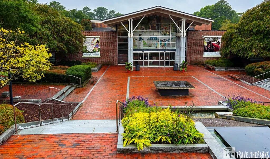 Entrance of the Colonial Williamsburg Visitor Center with brick and glass facade, surrounded by gardens and a red brick pathway.