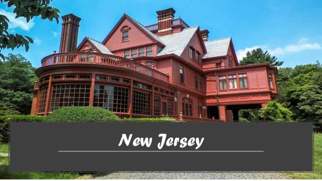 A large red Victorian mansion-Thomas Edison residence with a round turret, lush greenery, and a blue sky.

