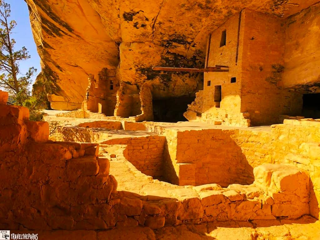 View of ancient stone dwellings and Kiva at Balcony House, Mesa Verde, under a large sandstone cliff.