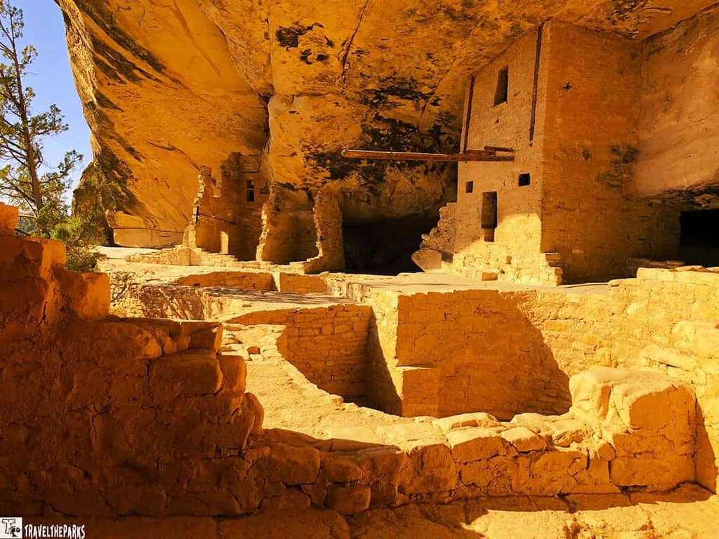 View of ancient stone dwellings and Kiva at Balcony House, Mesa Verde, under a large sandstone cliff.