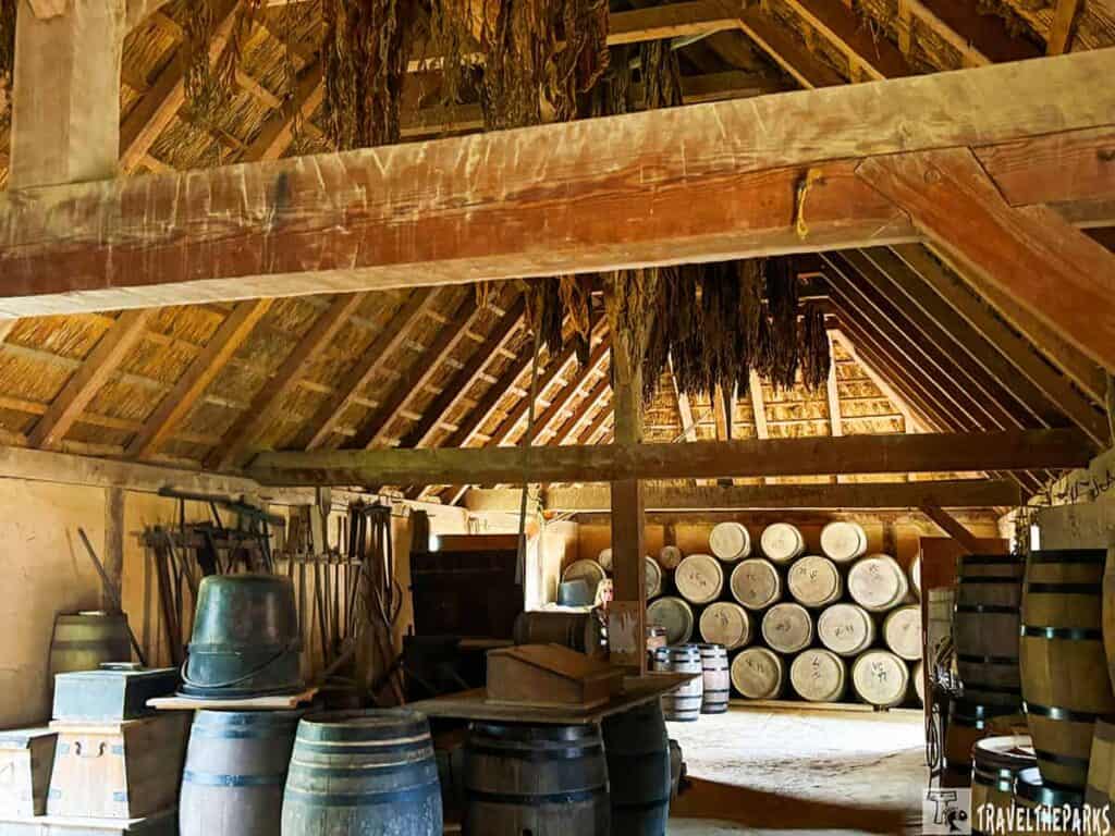 Interior of a historic wooden structure with a thatched roof and barrels at Jamestown Settlement.

