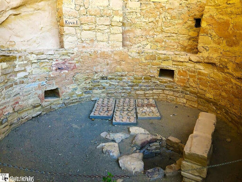 Circular stone kiva with walls and two rectangular grids in the floor.