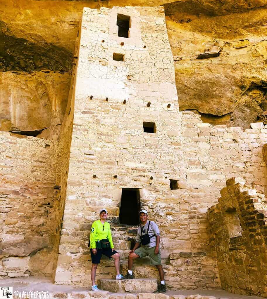 Two people stand in front of an ancient stone structure at Cliff Palace House Mesa Verde