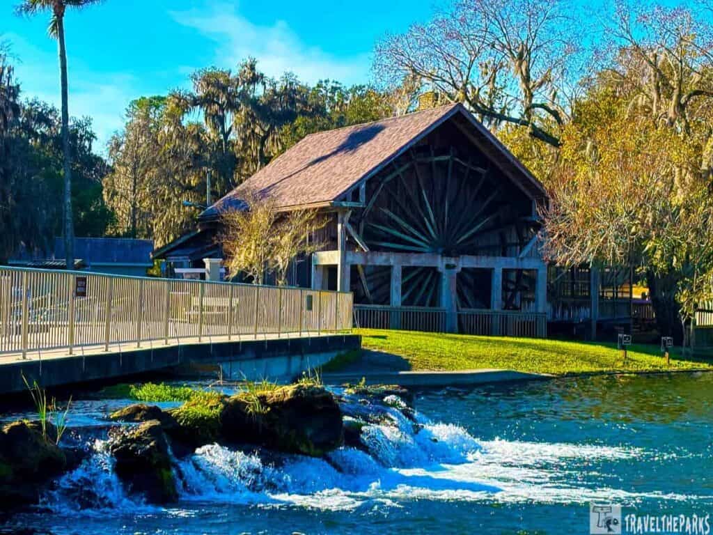 A rustic wooden structure by a flowing spring at Deleon Springs State Park, surrounded by trees.