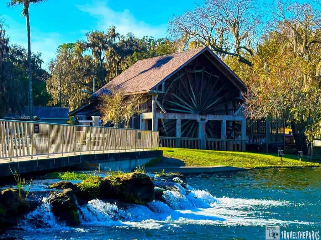 A rustic wooden structure by a flowing spring at Deleon Springs State Park, surrounded by trees.