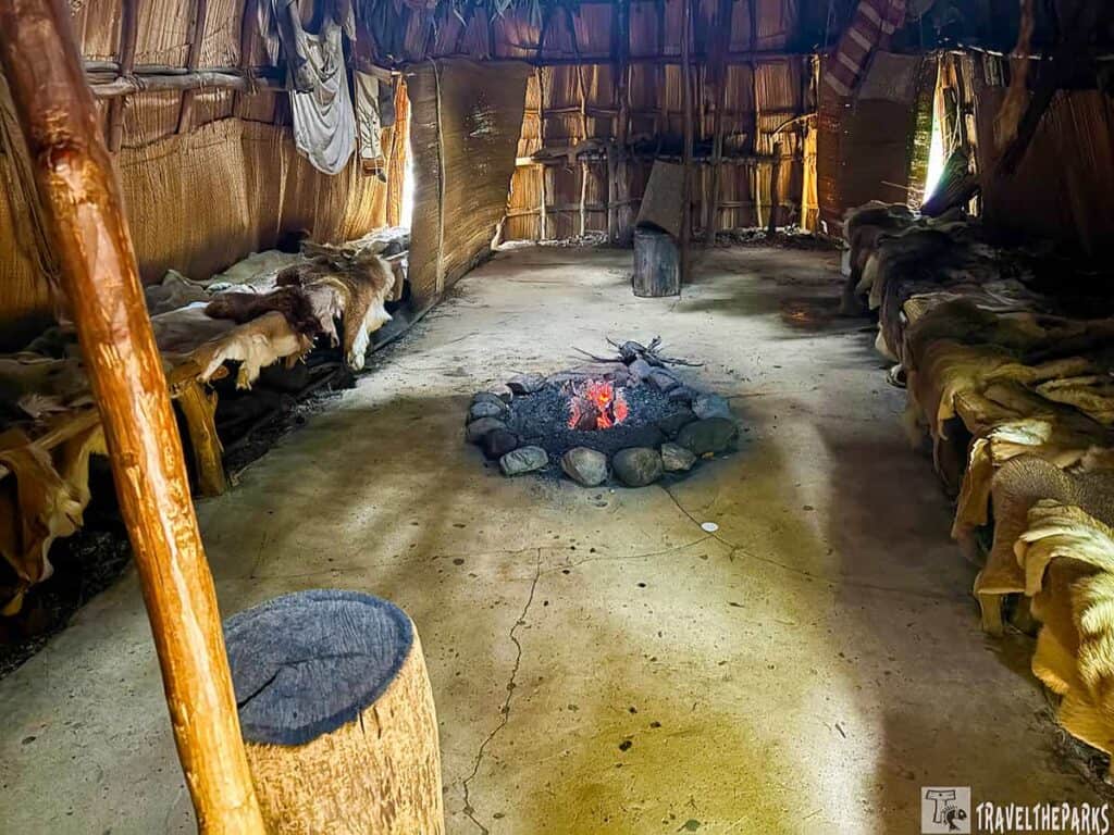Interior of a dome-shaped yahacan house with a central fire pit and benches covered in animal hides.

