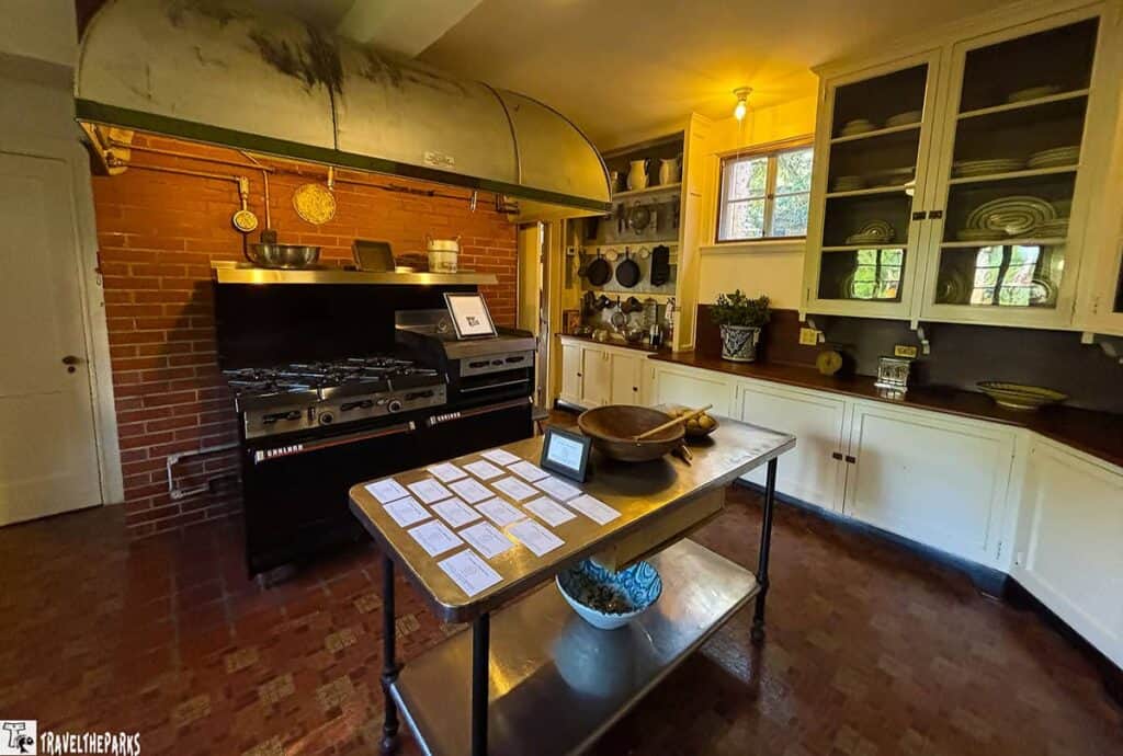 Interior of an old-fashioned kitchen with a brick wall, industrial stove, and metal table.

