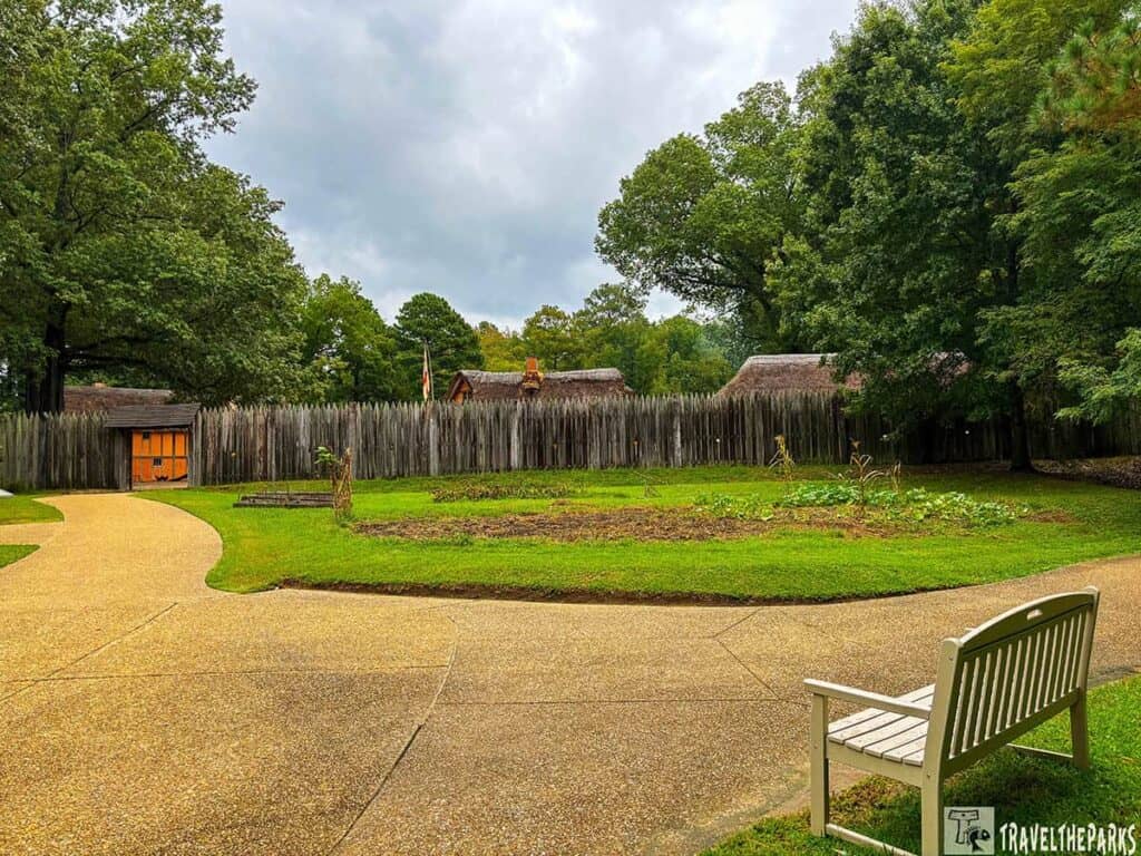 Outdoor view of Jamestown Settlement at James Fort with a winding pathway, wooden palisade fence, and surrounding trees.

