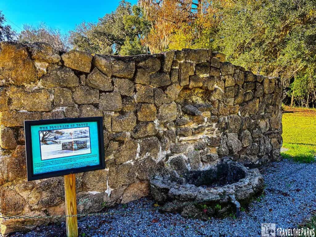 A stone wall and fountain at Deleon Springs State Park with an informational sign.

