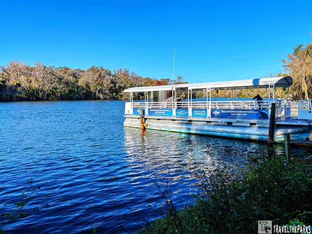 A boat with a covered roof docked on a blue body of water with trees in the background.

