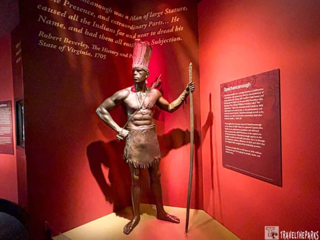 Museum exhibit showing a statue of Opechancanough with informational panels.

