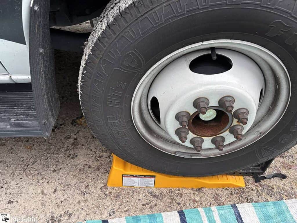 Close-up of a vehicle tire on a yellow leveling block on dirt.