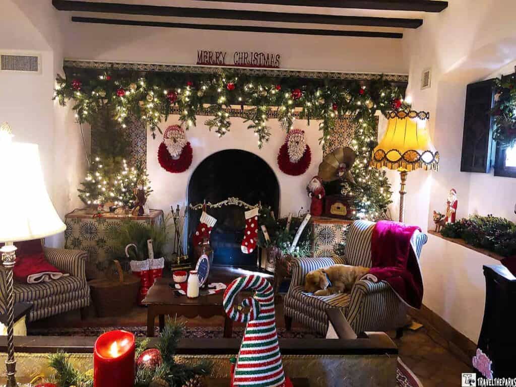 A living room decorated for Christmas with a fireplace, garland, stockings, and a sleeping dog on an armchair.

