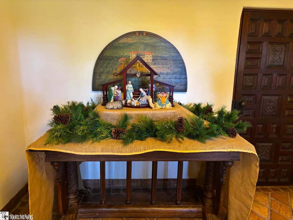 Nativity scene with pine garland on a decorated wooden table.

