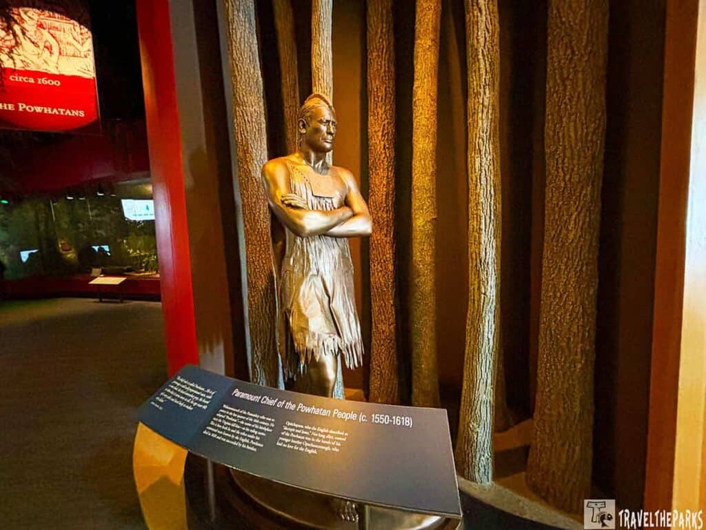 Bronze statue of a Native American man at Jamestown Settlement Museum exhibit with an information panel in front.

