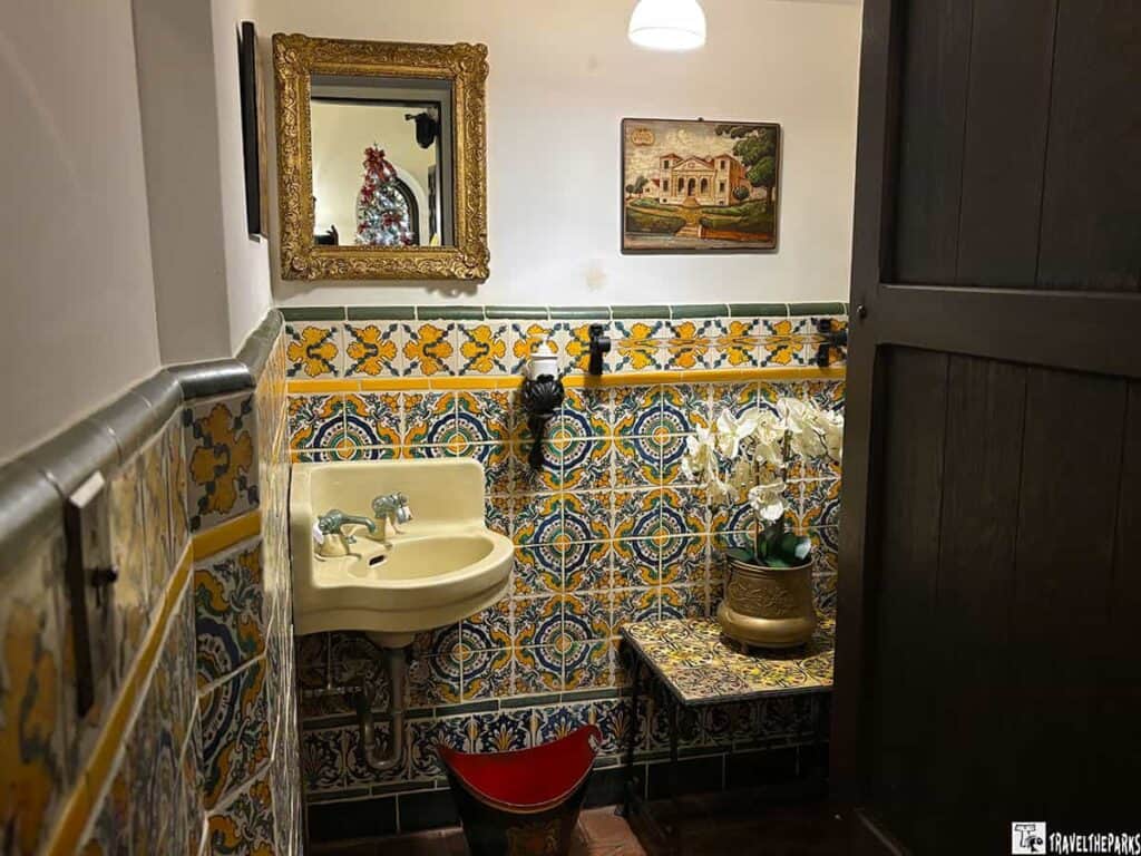 Ornate restroom with colorful tiles, a sink, mirror, and potted orchids.

