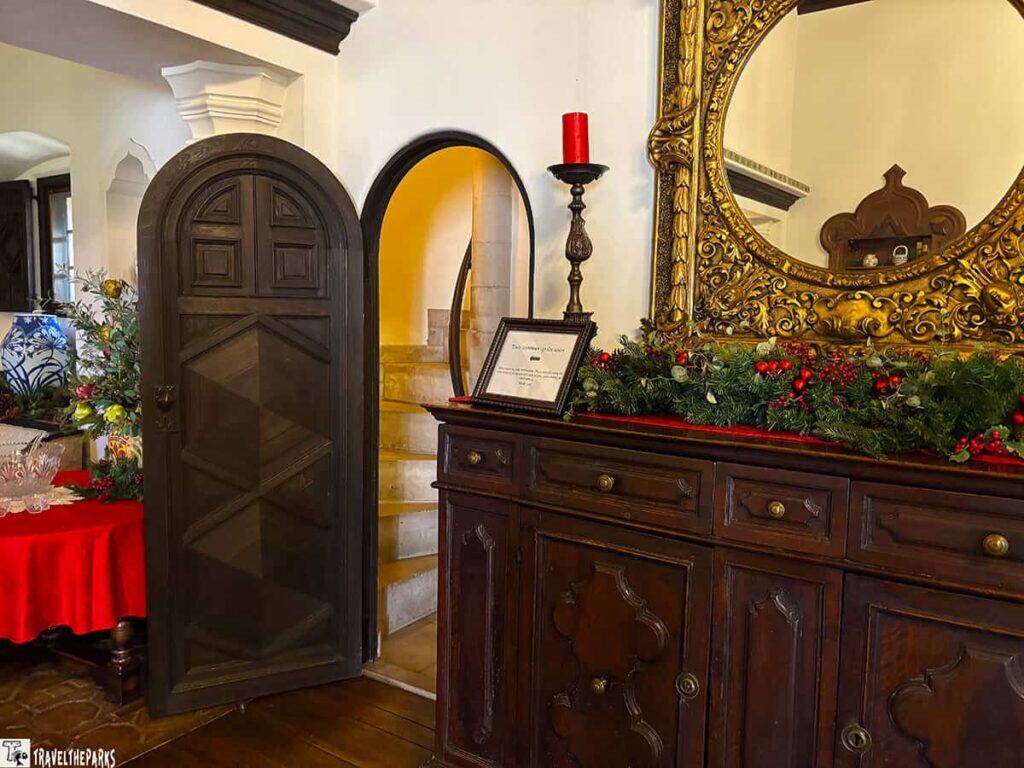 Interior of El Retiro mansion with a wooden door, spiral staircase, and decorated cabinet with a round mirror.

