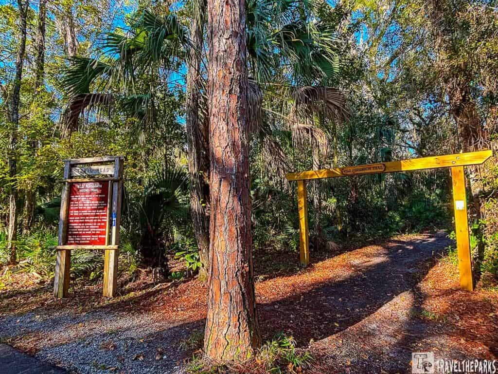 Entrance to Wild Persimmon Trail at Deleon Springs State Park with wooden sign and archway amidst lush greenery.

