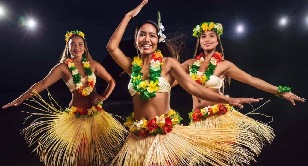 At night at the Royal Lahaina Luau in Maui, three women in colorful Hawaiian dresses dance, embodying the spirit of the vibrant valley isle.