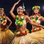 At night at the Royal Lahaina Luau in Maui, three women in colorful Hawaiian dresses dance, embodying the spirit of the vibrant valley isle.