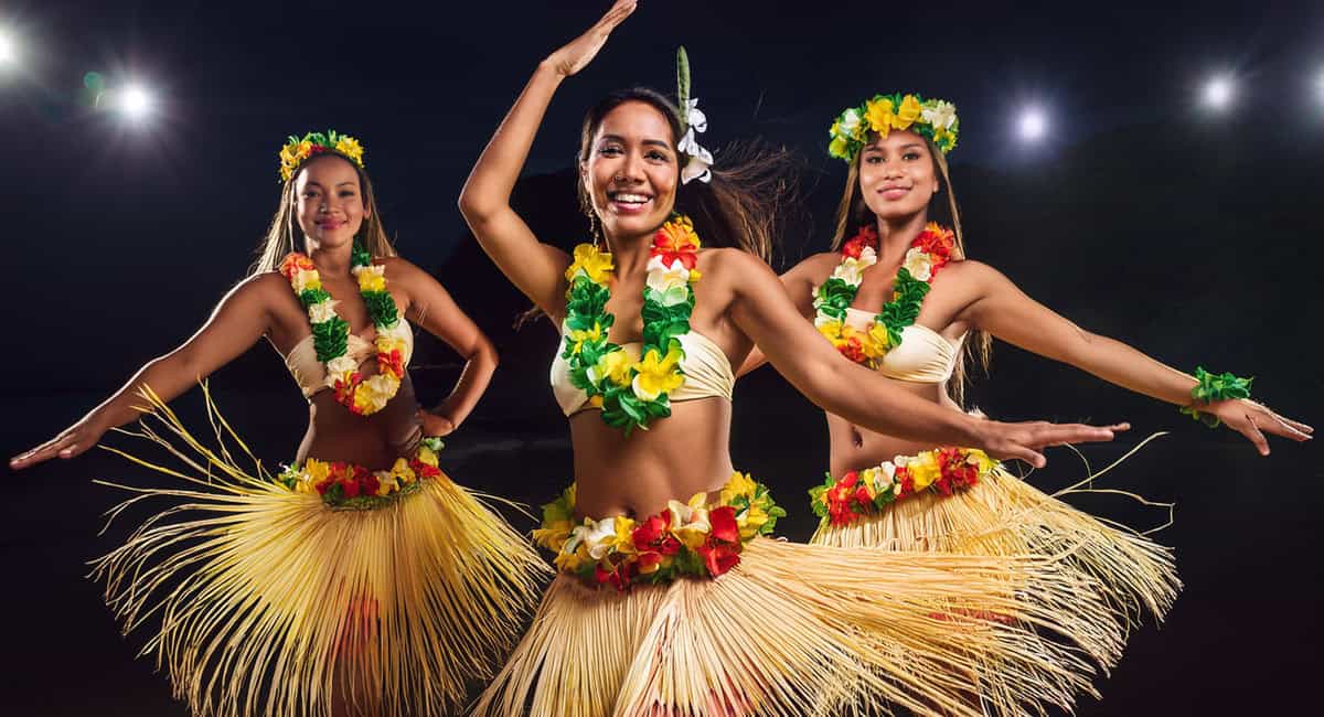 At night at the Royal Lahaina Luau in Maui, three women in colorful Hawaiian dresses dance, embodying the spirit of the vibrant valley isle.