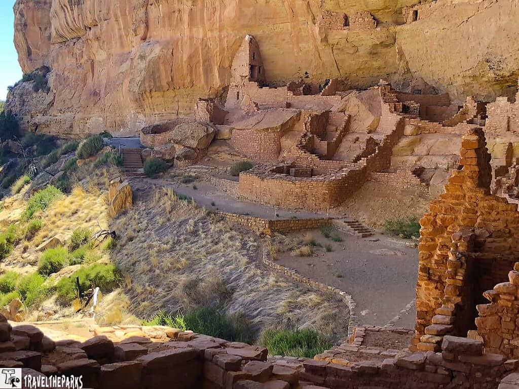 Longhouse cliff dwelling built into a sandstone cliff with multiple stone rooms and a scenic canyon view.
