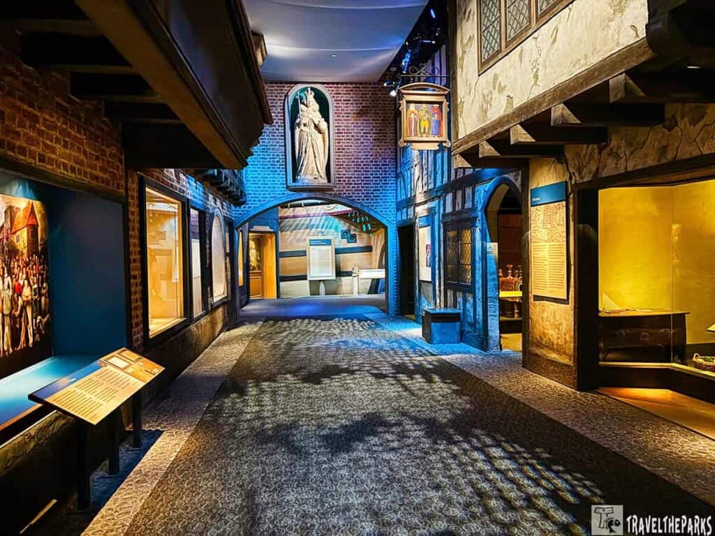 Interior view of a museum exhibit designed as a historical street, with brick and timber-framed walls, displays, and a statue above an archway.
