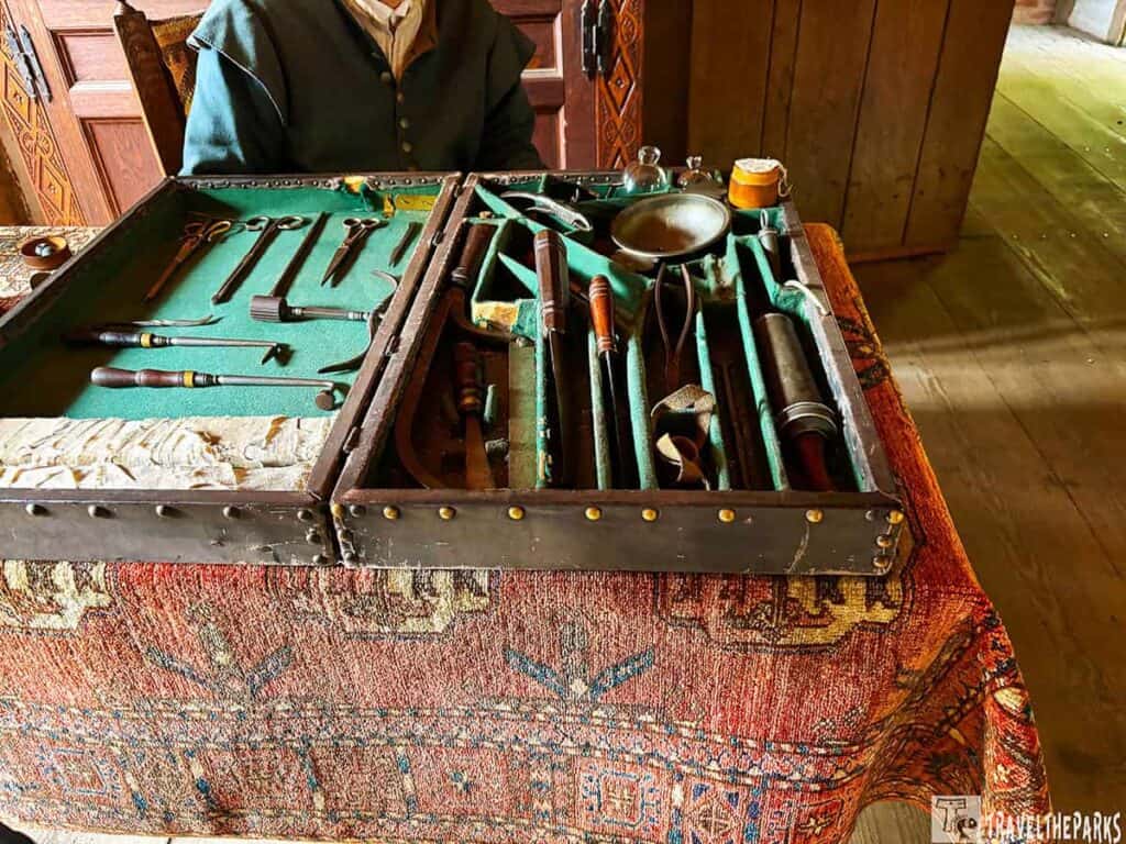 A display of historical surgical tools in a wooden box at Jamestown Settlement on a patterned rug.

