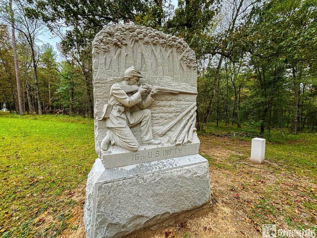 Stone monument of a Civil War soldier kneeling and aiming a rifle, labeled "16th U.S. INFTY," set in a wooded area.


