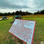 Two cannons on a grassy field with a historical plaque in the foreground.