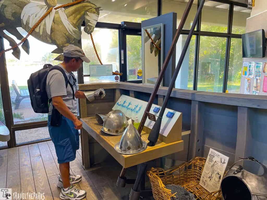 A man examines historical military items, including helmets and gauntlets, inside a visitor center.


